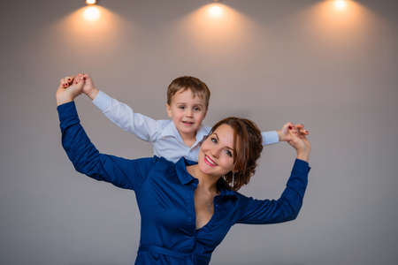 beautiful mother in a dress holds her son on her backの写真素材