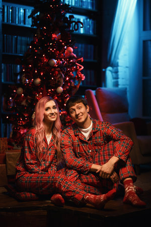 a man and a woman in red pajamas are sitting at night near the christmas treeの写真素材