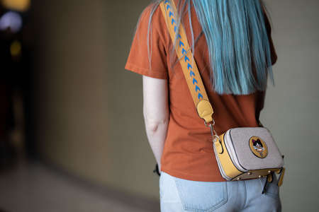 a woman with blue hair stands with her back, and on her shoulder she has a small yellow bag with a...