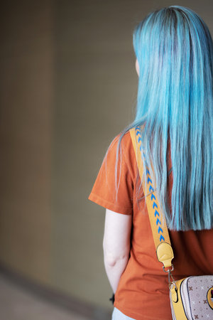 a woman with blue hair stands with her back, and on her shoulder she has a small yellow bag with a picture of a catの写真素材
