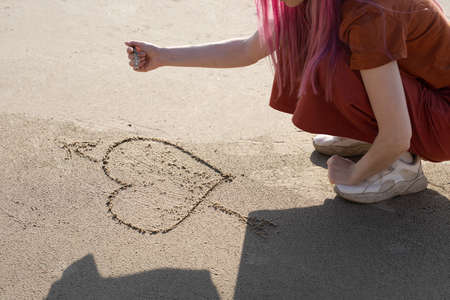 woman with pink hair draws a heart with a stick on the sandの写真素材