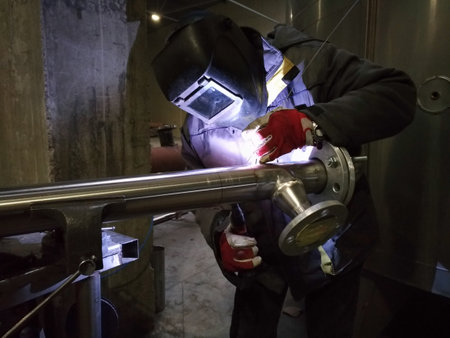 TIG welding process with welder in protective gear joining a metal pipe. Close-up of arc and tools