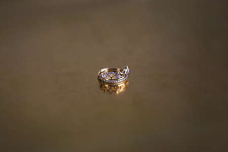 Golden ring with precious stones on a golden glossy backgroundの写真素材