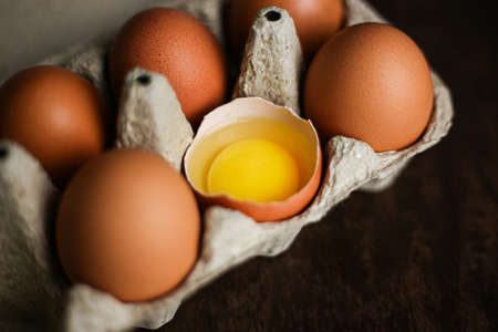 Fresh brown eggs and a broken egg with yolk in an eco tray made from recycled paper on a dark wooden backgroundの写真素材