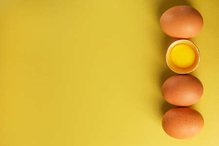 Fresh brown eggs and a broken egg with yolk on a light yellow background with space for text, copy spaceの写真素材