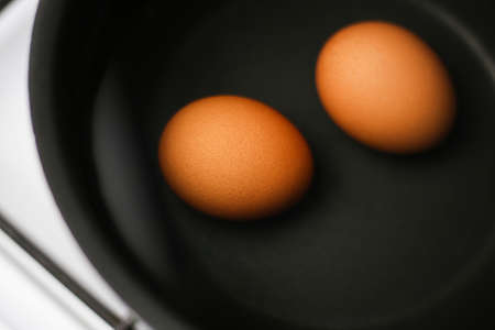 Two brown eggs in a pot of water on the stove