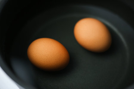 Two brown eggs in a pot of water on the stoveの写真素材
