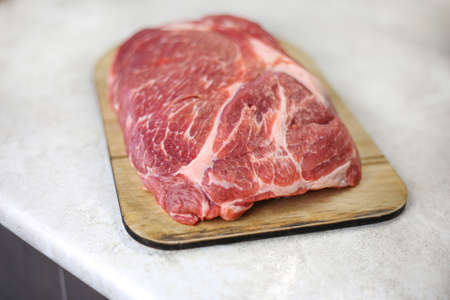 Big fresh piece of meat on wooden cutting board on light kitchen tableの写真素材