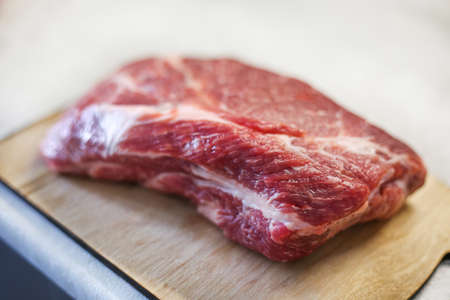 Big fresh piece of meat on wooden cutting board on light kitchen tableの写真素材