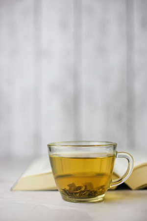 Brewed herbal green tea in a transparent cup in front of an open book on a light backgroundの写真素材