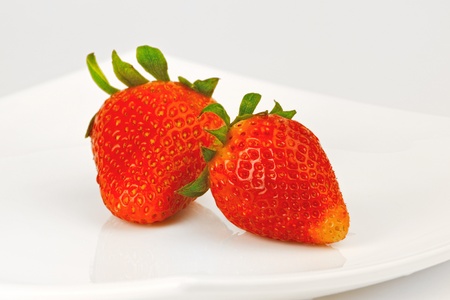 Two berries of strawberry on a white plateの写真素材