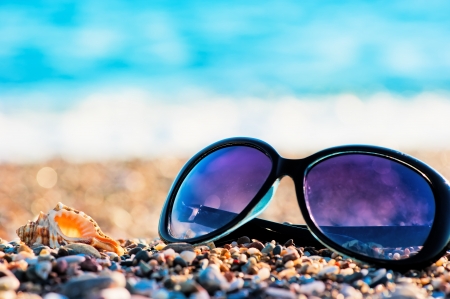 Sunglasses and shells lie on the shingle beach seaの写真素材