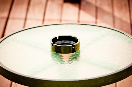 black empty ashtray stands in the middle of a round glass tableの写真素材