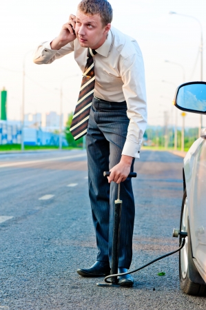 businessman pumps the pump wheel of a car and talking on the phoneの写真素材