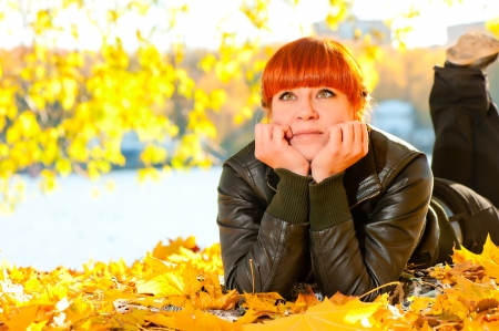 beautiful girl with red hair in leaves in autumn parkの写真素材