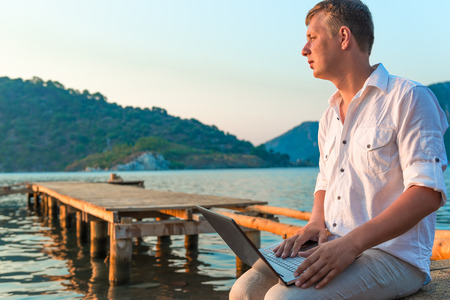 man in a white shirt with a laptop on the pier to meet a dawnの写真素材