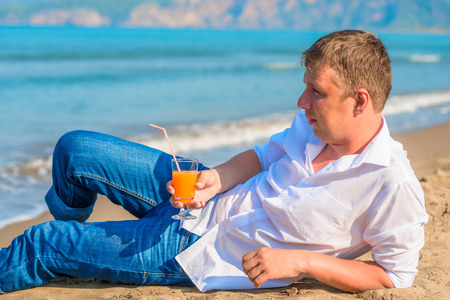 a man lies with a cocktail on the sandy beach in clothesの写真素材
