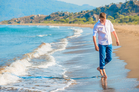 man in jeans and a white shirt walking along the seashoreの写真素材