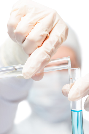 Chemist hands in rubber gloves pour hazardous liquids into test tubes close-upの写真素材