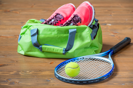 Racket and ball for tennis in focus on the background of bag with sneakers on the floorの写真素材