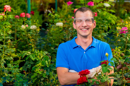 Happy man with glasses and laboratory gloves in a greenhouse among flowersの写真素材