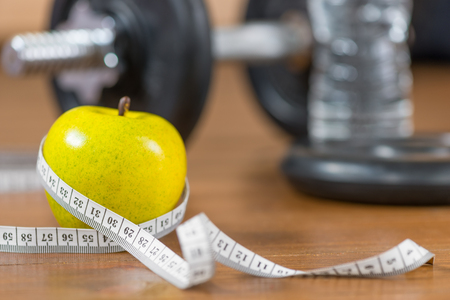 Fresh apple and centimeter close-up in the gym on the floor against a dumbbell backgroundの写真素材