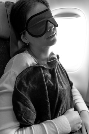 Girl under a rug with a mask in her eyes asleep on the plane, black and white photoの写真素材