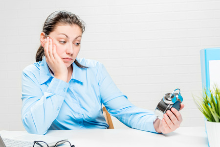 Tired businesswoman looks at the alarm clock and waits for the end of the working dayの写真素材