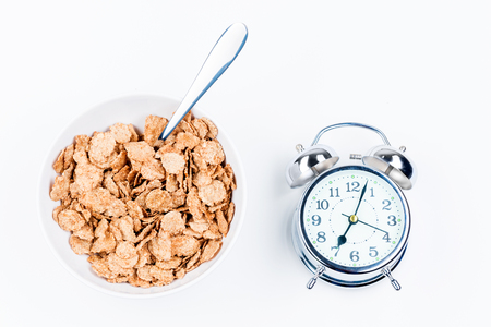 A plate of useful muesli for breakfast and a retro alarm clock on a white background close-upの写真素材