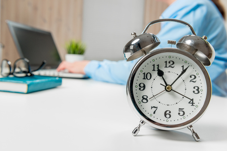 Businesswoman working in the office, in focus, an alarm clock on a close-up tableの写真素材