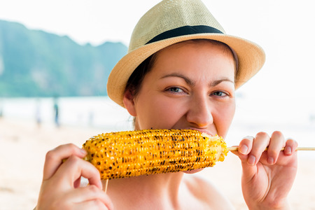 portrait of a woman with a delicious corn grill on the beachの写真素材