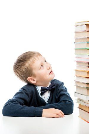 the schoolboy looks at the heap of books on the tableの写真素材