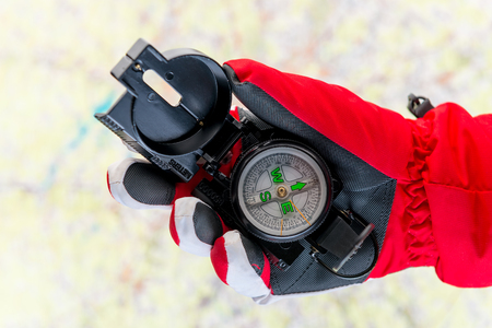 conceptual photo - search for missing tourists in the mountains in winter - a hand in the glove holds a compass on the background of the mapの写真素材