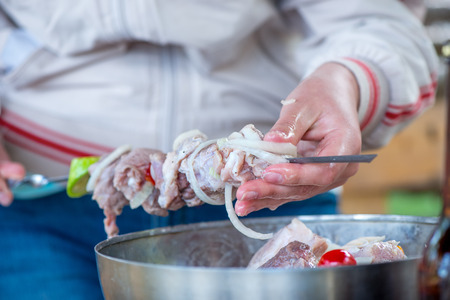 woman preparing shish kebab, close-up of hands, skewer and meatの写真素材