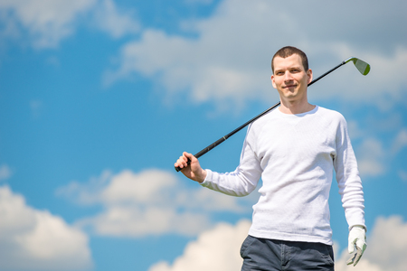 horizontal portrait of a successful golfer with a golf club on a blue sky backgroundの写真素材