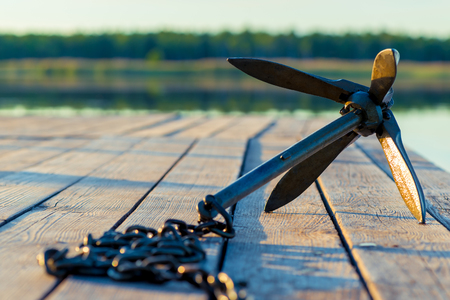 A heavy anchor with a chain in the rays of the morning sun lies on a wooden pierの写真素材