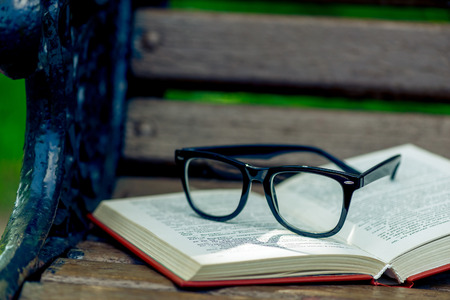 open book and black stylish glasses on a wooden bench in the park, close-up photoの写真素材