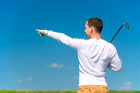 the golfer shows his hand the trajectory of the flight of his ball on the fieldの写真素材