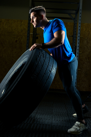 strong young athlete with a large heavy wheel in the gymの写真素材
