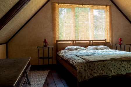 bed near a window in a room on the top floor of a wooden house, under a roofのeditorial素材