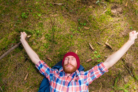 thoughtful hipster stroking his red beard, a portrait of a curtain, a man lying on the ground in the forestの写真素材
