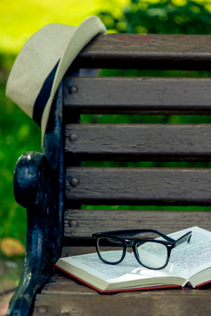 an interesting book, glasses and a beige straw hat were left on a bench in the parkの写真素材