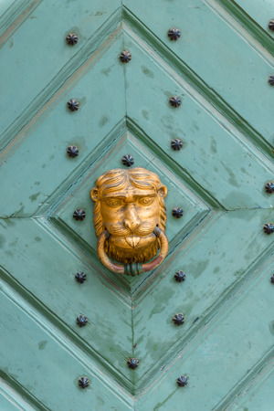 old wooden door with a brass handle in the shape of a lion's head close-upの写真素材