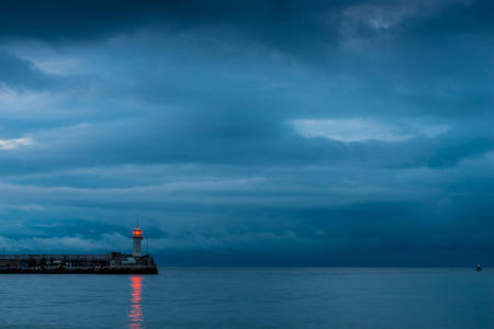 Beautiful lighthouse on the seashore at dusk, rainy clouds over the seaの写真素材