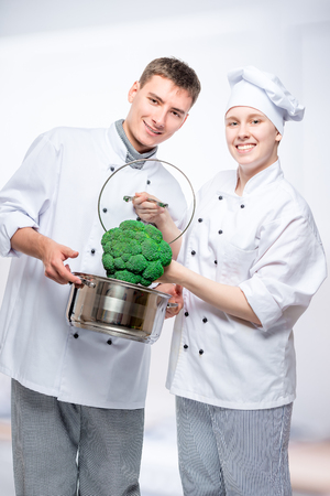 vertical portrait of fellow cooks with saucepan and broccoli in a commercial kitchenの写真素材