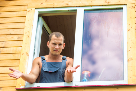 Discouraged man in overalls reflects on washing the window in the houseの写真素材