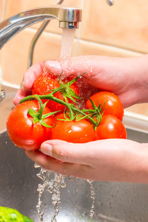 washing a tomato in the kitchen under running water, hands close upの写真素材