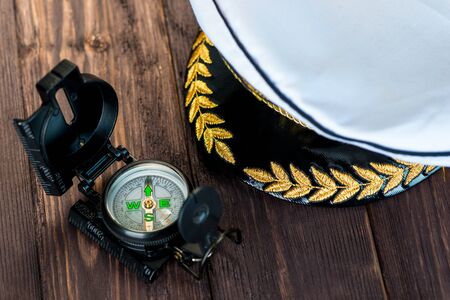 cap of the ship captain and next to it lies a compass on a wooden tableの写真素材