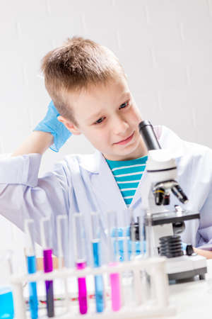 A schoolboy with a microscope examines chemicals in test tubes, conducts experiments - a portrait on...
