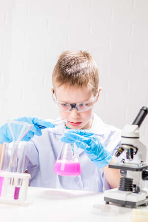 A schoolboy with a microscope examines chemicals in test tubes, conducts experiments - a portrait on...